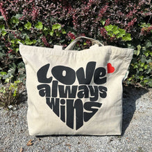 Afbeelding in Gallery-weergave laden, Duurzame met hart van gerecycled katoen tekst Love Always Wins foto buiten op grindpad
